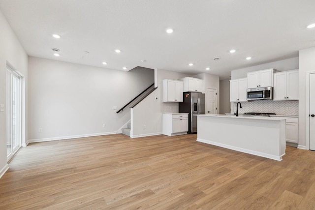 kitchen with stainless steel appliances, white cabinetry, a kitchen island with sink, and light hardwood / wood-style floors