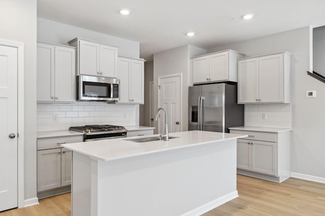 kitchen with sink, light hardwood / wood-style flooring, stainless steel appliances, an island with sink, and decorative backsplash