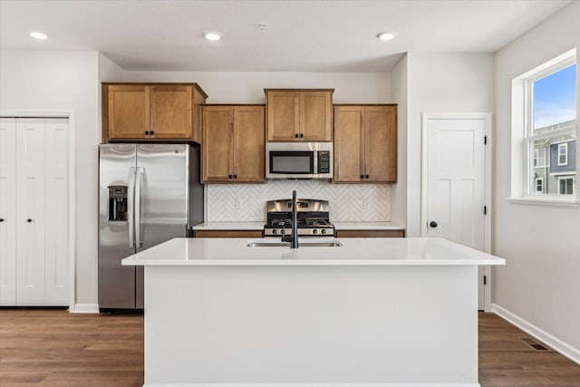 kitchen with stainless steel appliances, an island with sink, tasteful backsplash, and dark hardwood / wood-style flooring