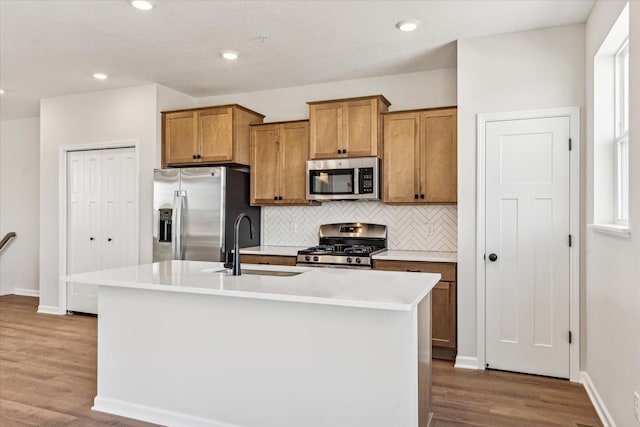 kitchen featuring an island with sink, appliances with stainless steel finishes, sink, and wood-type flooring