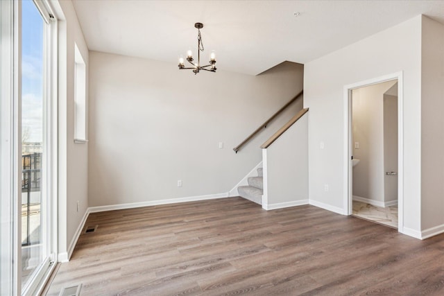 spare room with a notable chandelier, wood-type flooring, and a wealth of natural light