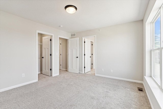 unfurnished bedroom featuring multiple windows, a spacious closet, a closet, and light carpet