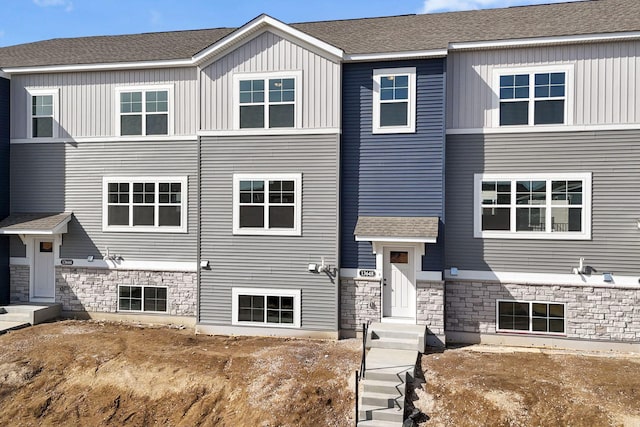 view of front of house with stone siding, roof with shingles, and board and batten siding