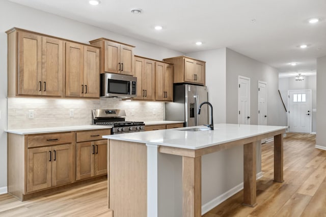 kitchen with light hardwood / wood-style flooring, sink, a kitchen island with sink, decorative backsplash, and stainless steel appliances