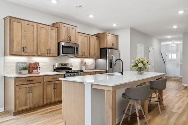 kitchen featuring a breakfast bar, a sink, light countertops, appliances with stainless steel finishes, and an island with sink