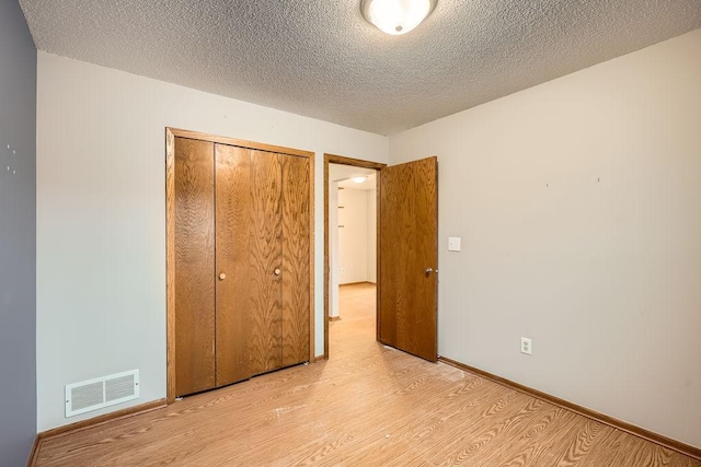 unfurnished bedroom with a textured ceiling, light hardwood / wood-style flooring, and a closet