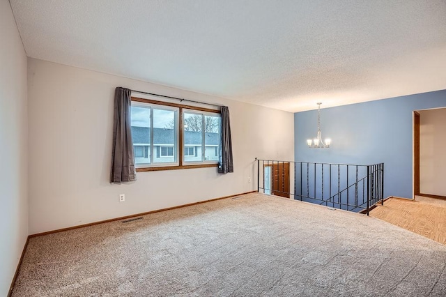 carpeted empty room featuring a textured ceiling and a chandelier