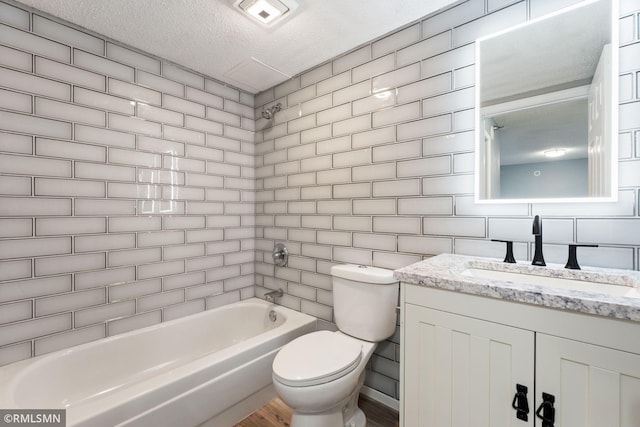 full bathroom with tiled shower / bath, vanity, toilet, and a textured ceiling