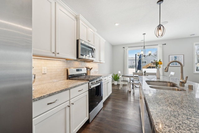 kitchen featuring pendant lighting, appliances with stainless steel finishes, sink, white cabinetry, and light stone counters