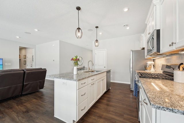 kitchen with pendant lighting, white cabinets, stainless steel appliances, sink, and a center island with sink