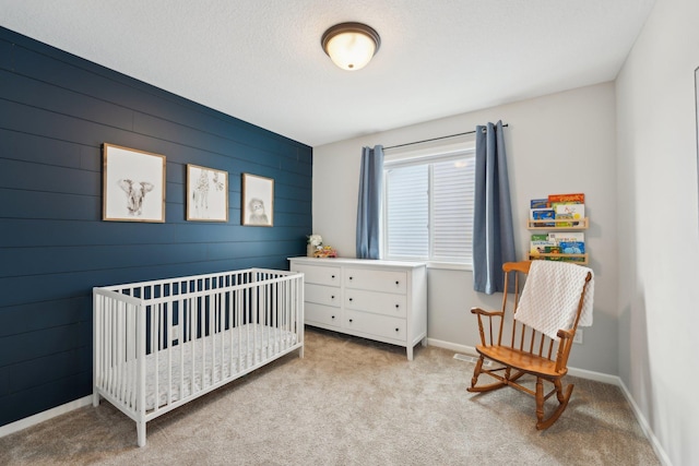 bedroom with a nursery area, a textured ceiling, and light carpet