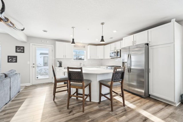 kitchen with stainless steel appliances, hanging light fixtures, white cabinets, and light wood-type flooring