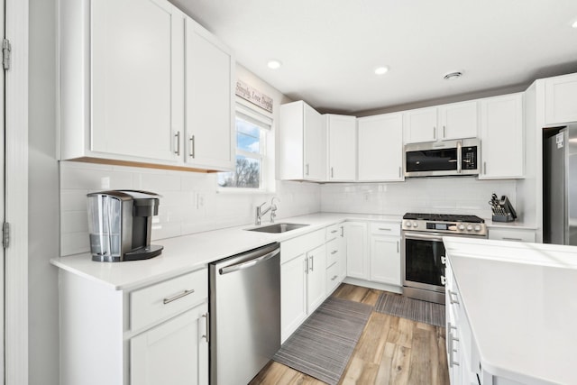 kitchen featuring sink, white cabinetry, tasteful backsplash, appliances with stainless steel finishes, and light hardwood / wood-style floors