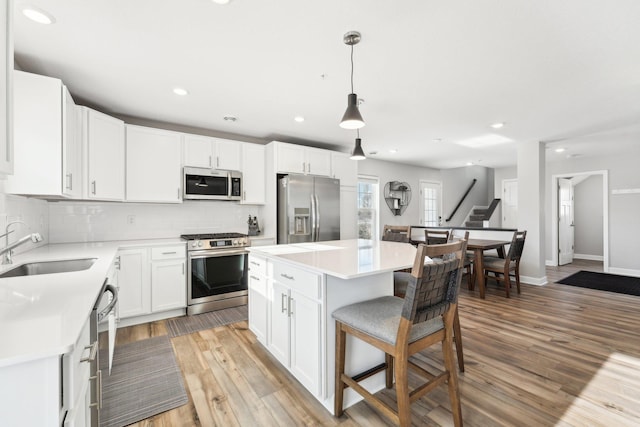 kitchen featuring appliances with stainless steel finishes, sink, white cabinets, hanging light fixtures, and a center island