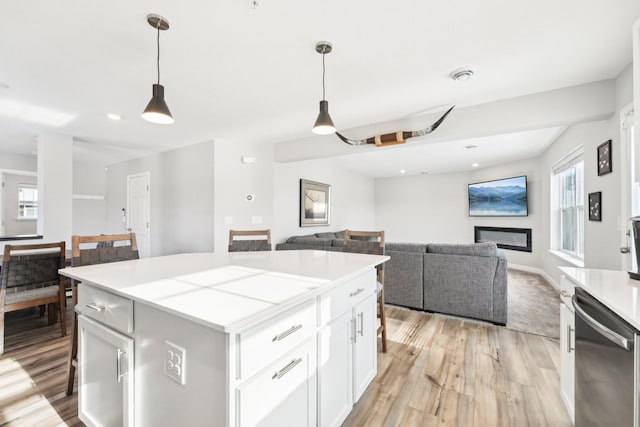 kitchen featuring a center island, light hardwood / wood-style flooring, stainless steel dishwasher, pendant lighting, and white cabinets