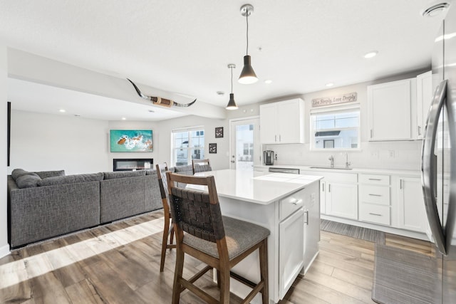 kitchen featuring stainless steel refrigerator, white cabinets, hanging light fixtures, a center island, and light wood-type flooring