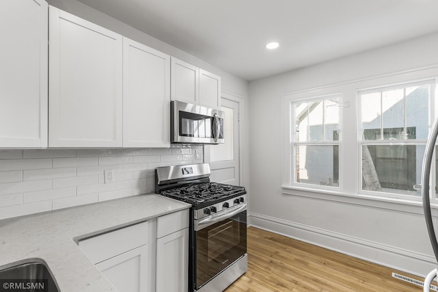 kitchen featuring appliances with stainless steel finishes, light stone counters, white cabinetry, and light hardwood / wood-style floors