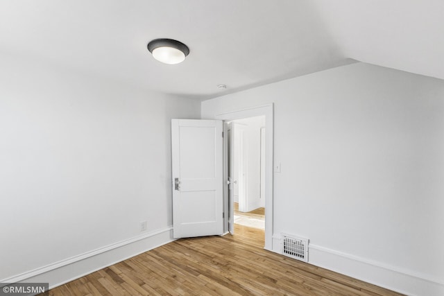 empty room with light wood-type flooring and vaulted ceiling