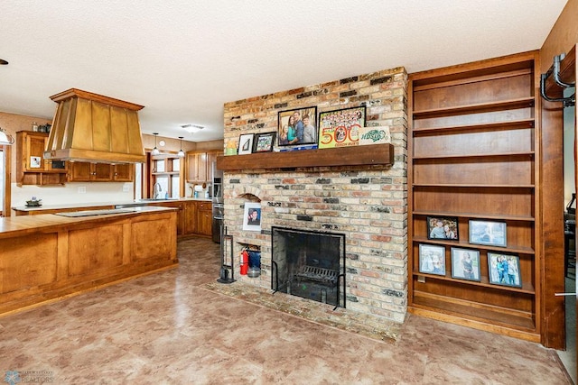 kitchen featuring stovetop, hanging light fixtures, a textured ceiling, island exhaust hood, and a brick fireplace