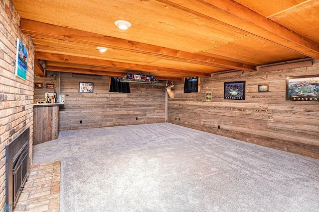 interior space with wooden walls, carpet, wood ceiling, a brick fireplace, and beam ceiling