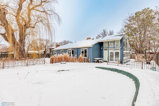 snow covered rear of property with a sunroom