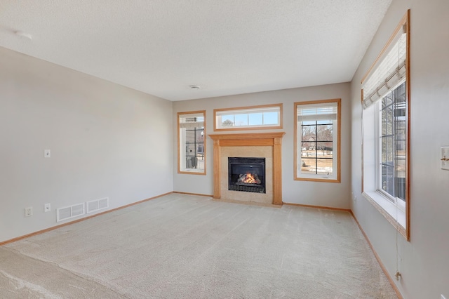 unfurnished living room with light carpet, a textured ceiling, a fireplace with flush hearth, and visible vents