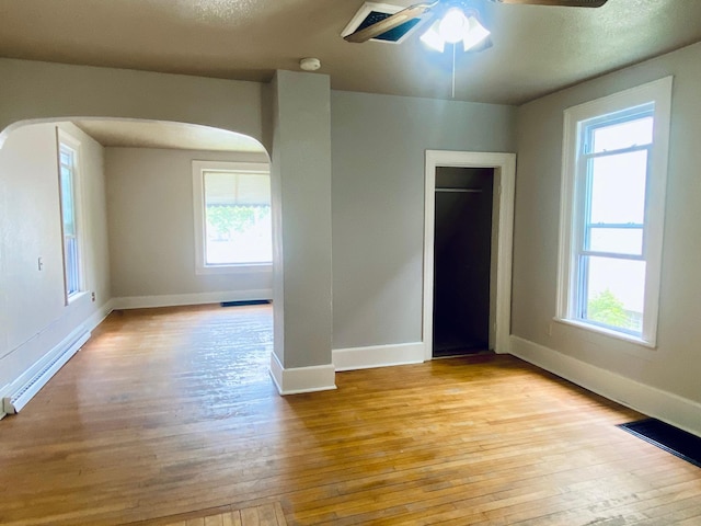 unfurnished bedroom with light wood-type flooring, ceiling fan, baseboard heating, and multiple windows