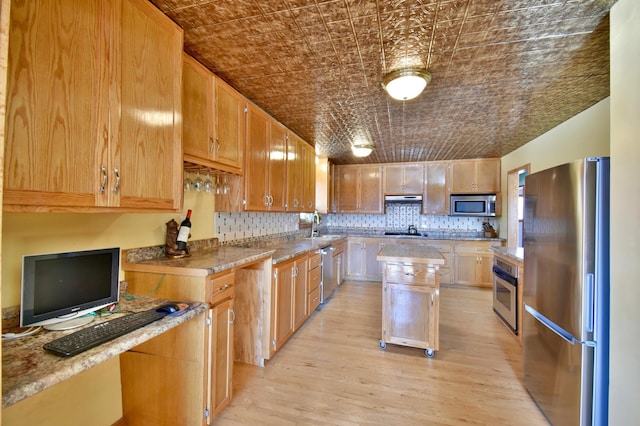 kitchen with sink, stainless steel appliances, light stone countertops, a kitchen island, and light wood-type flooring