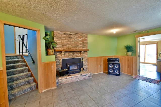 unfurnished living room with light tile patterned floors, wooden walls, a textured ceiling, and a wood stove