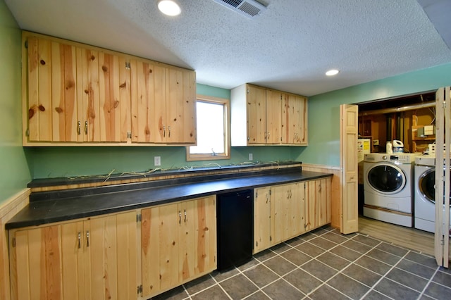 kitchen with light brown cabinetry, dark tile patterned flooring, a textured ceiling, and washing machine and clothes dryer