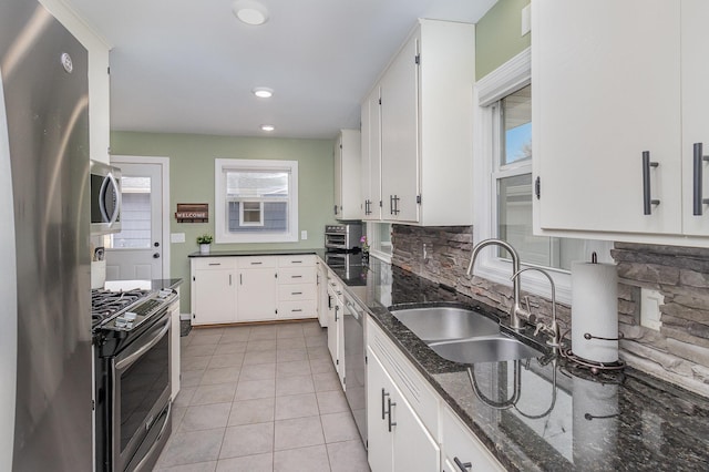 kitchen featuring light tile patterned flooring, stainless steel appliances, a sink, white cabinets, and tasteful backsplash