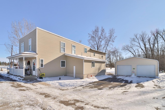 snow covered rear of property featuring covered porch, an outdoor structure, and a garage