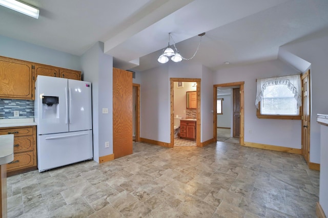 kitchen with decorative backsplash, brown cabinetry, a chandelier, and white refrigerator with ice dispenser
