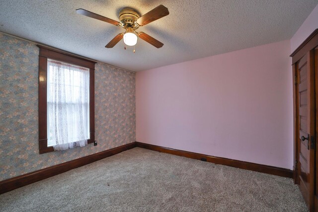 unfurnished room featuring carpet flooring, a textured ceiling, baseboards, wallpapered walls, and a ceiling fan