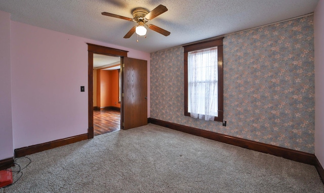 empty room featuring wallpapered walls, ceiling fan, carpet, and a textured ceiling