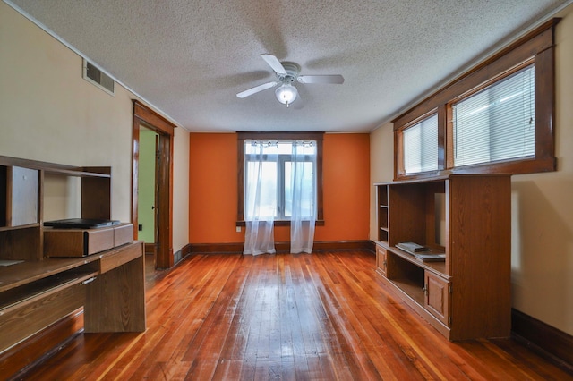 unfurnished living room featuring a textured ceiling, baseboards, visible vents, ceiling fan, and hardwood / wood-style floors