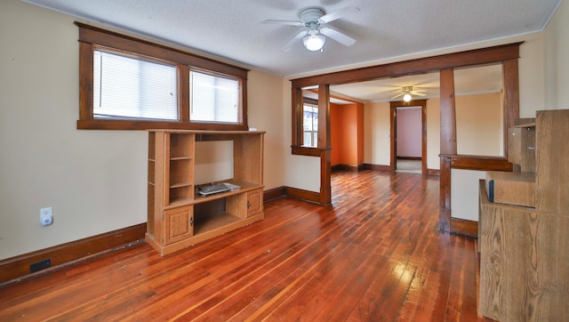 unfurnished living room featuring a ceiling fan, a textured ceiling, baseboards, and dark wood finished floors