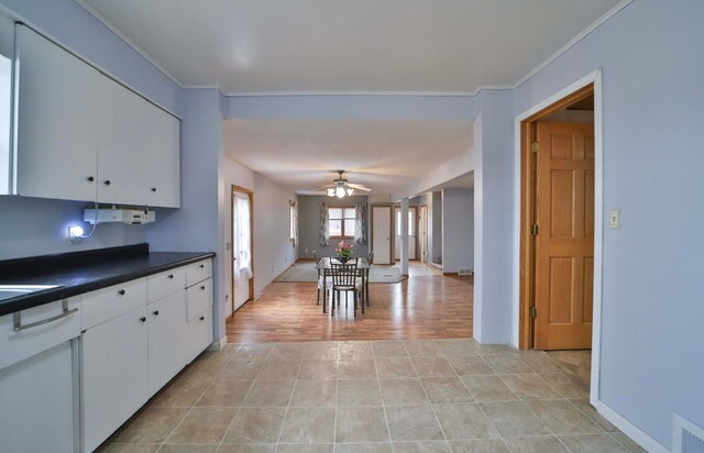 kitchen with crown molding, light tile patterned floors, dark countertops, white cabinets, and ceiling fan