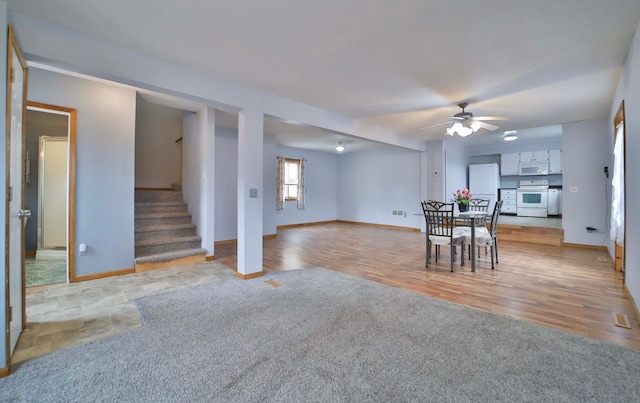 unfurnished dining area featuring a ceiling fan, stairs, baseboards, visible vents, and light wood-style flooring