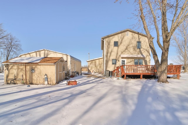 snow covered rear of property featuring an outdoor structure, a storage shed, and a wooden deck