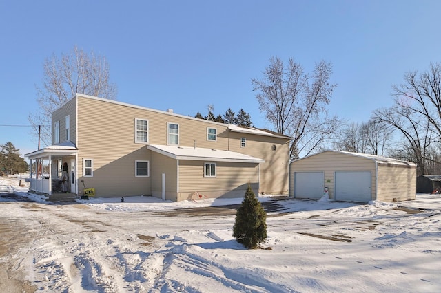 snow covered back of property featuring a garage and an outdoor structure