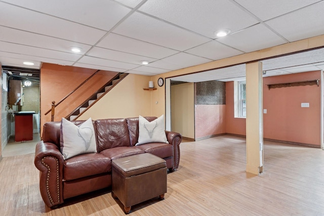 living room with light wood-style flooring, stairs, a drop ceiling, and baseboards