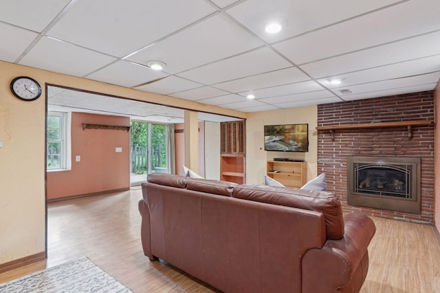 living area with light wood-type flooring, a drop ceiling, baseboards, and a brick fireplace