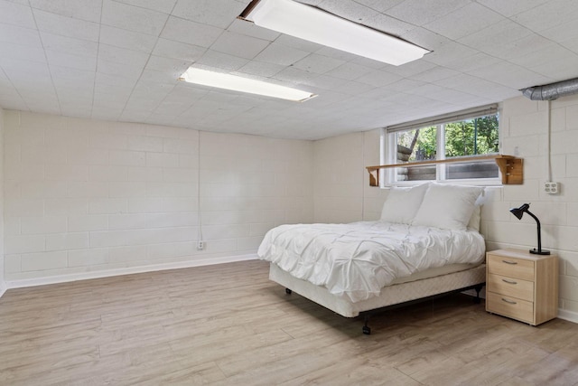 bedroom with light wood finished floors and concrete block wall