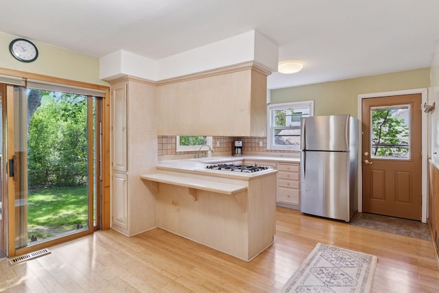 kitchen with freestanding refrigerator, light countertops, white gas cooktop, and light brown cabinets