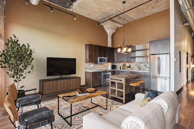 living room with sink, hardwood / wood-style flooring, a towering ceiling, track lighting, and a chandelier