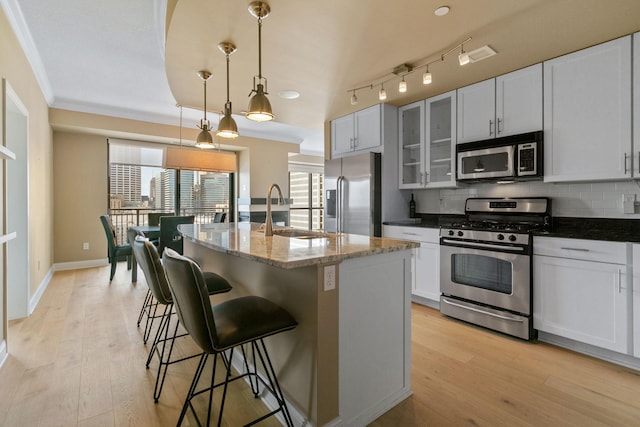 kitchen featuring appliances with stainless steel finishes, decorative light fixtures, sink, backsplash, and a kitchen island with sink