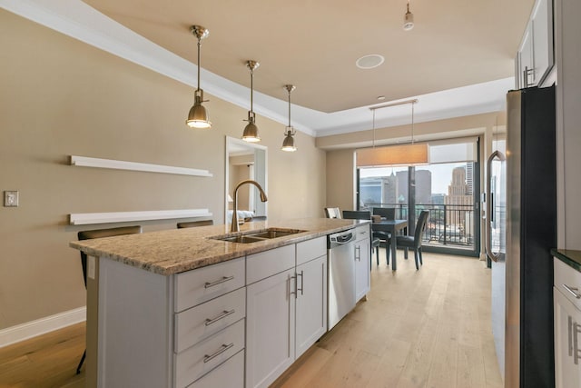 kitchen featuring appliances with stainless steel finishes, sink, white cabinets, light stone counters, and a center island with sink