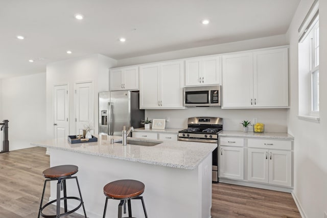 kitchen with white cabinets, stainless steel appliances, a kitchen island with sink, and sink