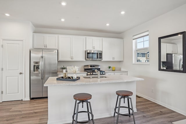 kitchen with hardwood / wood-style flooring, white cabinets, a breakfast bar, stainless steel appliances, and a center island with sink